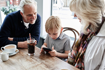 Family, grandparents and kid with phone at cafe for online games, e learning and streaming video...