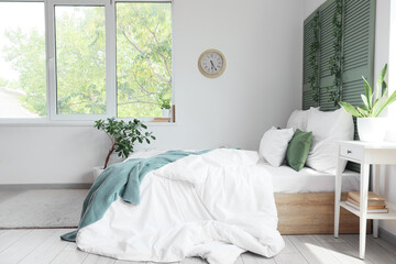 Interior of light bedroom with green folding screen and plants