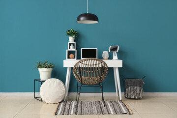 Modern table with laptop, tablet and houseplant near blue wall in room