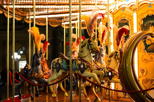 Colorful carousel horses with feathers in nighttime amusement park.