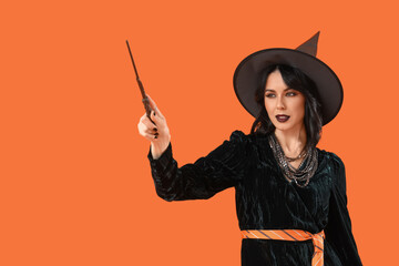 Beautiful young woman dressed as witch for Halloween with magic wand on orange background