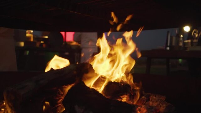 Toma orbital en slow motion de la brasa de una fogata con gente de fondo en la noche.