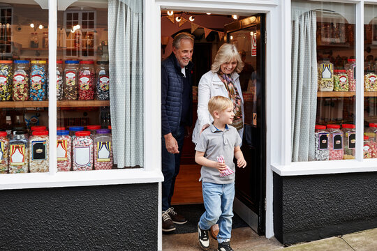Man, woman and child on street by candy shop for product, shopping and choice for love, care or bonding. Grandparents, boy kid and retail store with walk for sweets, sidewalk or dessert with family