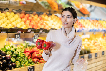 While shopping in vegetable store, female customer purchase fresh bell pepper. Wide range of agricultural products. Self-service, comfortable shopping.