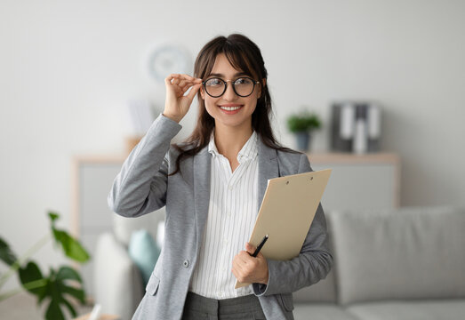 Successful psychologist. Portrait of arab female psychologist holding clipboard, smiling at camera in modern office. Confident psychoanalyst posing at mental health clinic