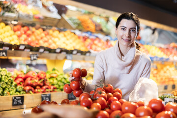 Young woman buyer choosing fresh tomatoes in vegetable shop