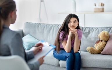 Female psychologist consulting depressed Indian teenage girl at office. Counsellor working with...