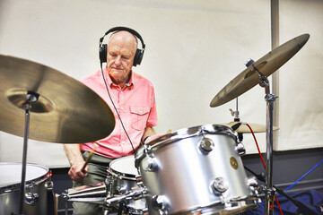 Senior man playing the drums with headphones in a music studio for recording a song, track or album...