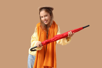 Cute teenage girl with red umbrella on brown background