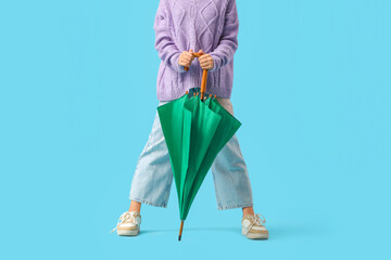 Teenage girl with green umbrella on blue background