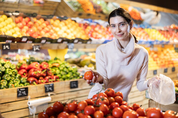 Young woman buyer choosing fresh tomatoes in vegetable shop