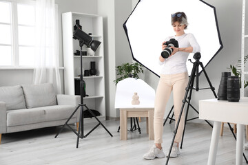 Beautiful young happy female photographer with professional camera and lighting working in studio