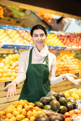 In sales hall of vegetable shop, visitors are greeted by seller woman. Staff at workplace willing to help, offering consultation and assistance.
