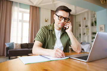 Obraz premium Focused individual engages in work while on a phone call in a bright, modern living space with stylish decor