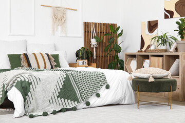 Interior of stylish bedroom with shelving unit, different houseplants and big bed