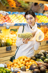 Young woman buyer choosing fresh papaya in vegetable shop