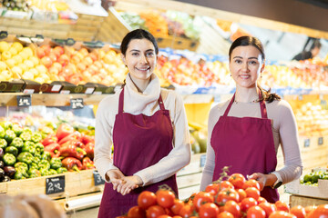 Young and adult women sellers offer fresh tomatoes in vegetable shop