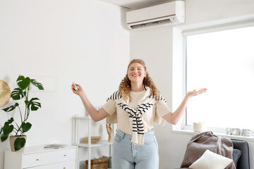 Beautiful smiling woman switching on air conditioner in living room