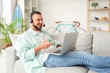 Young man with headset using laptop for online work at home