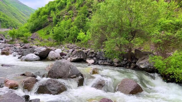 A beautiful river flowing through rocky terrain, surrounded by lush greenery in a mountain landscape. Perfect for content related to eco-tourism, nature documentaries, and outdoor adventures. Ideal fo