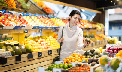 Young woman buyer choosing fresh avocados in vegetable shop