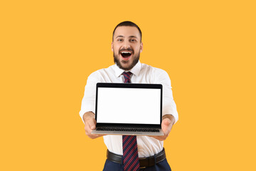 Happy young businessman with blank laptop on yellow background