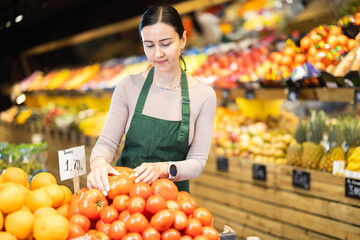 Supermarket employee carefully places ripe tomatoes on shelves of a grocery supermarket