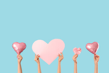 Female hands with heart-shaped balloons, paper heart and gift box on blue background. Valentine's...