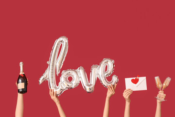 Female hands with balloon in shape of word LOVE, envelope, glasses and bottle of champagne on red background. Valentine's day celebration
