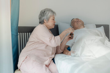 Obraz premium An elderly woman tends to her husband by administering medication while he rests in bed. The image emphasizes caregiving, compassion, and elderly support in a peaceful home setting.
