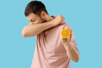 Sick young man with orange on blue background. Food Allergy Awareness Month