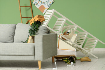 Interior of messy living room with grey sofa, overturned shelving unit and scattered belongings...