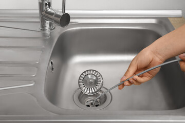 Woman cleaning drain with plumber's snake, closeup