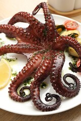 Fried octopus with herb sauce, lemon and vegetables on wooden table, closeup