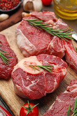 Pieces of raw beef, rosemary and tomato on wooden table, closeup