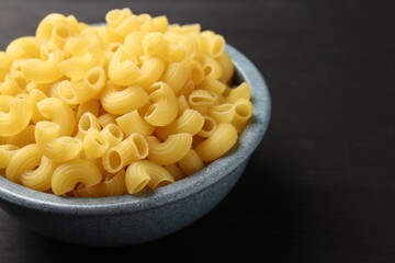 Raw horns pasta in bowl on dark table, closeup