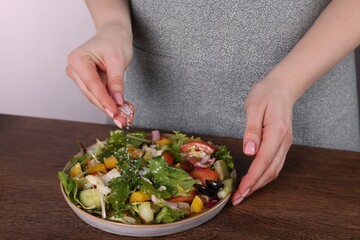 Woman salting tasty salad at wooden table against white background, closeup
