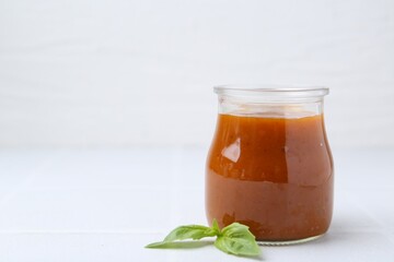 Tasty curry sauce in glass jar and basil on white tiled table, closeup. Space for text