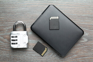 Hard disk drive, SD memory cards and combination padlock on grey wooden table, flat lay