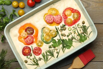 Raw focaccia with vegetables, spices and brush on wooden table, flat lay
