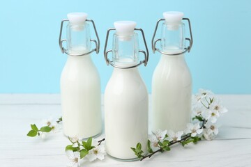 Fresh milk and blossoms on white table against light blue background