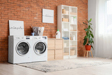 Interior of laundry room with modern washing machine and clothes dryer near brick wall