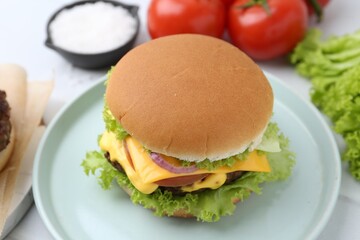 Tasty cheeseburger with lettuce and tomatoes on white table, closeup