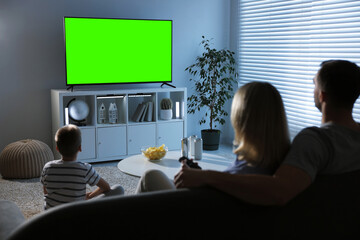 Family watching modern TV set with green screen at home. Chroma key compositing