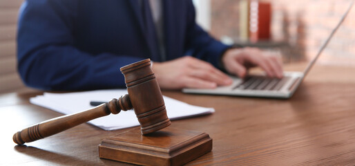 Closeup of judge working on laptop at wooden table, focus on gavel. Banner design