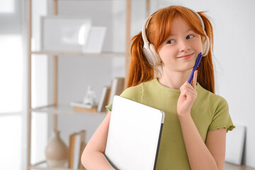 Little redhead student with laptop and headphones at home. Online education