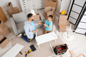 Cute boy with his father assembling shelf unit at home, top view