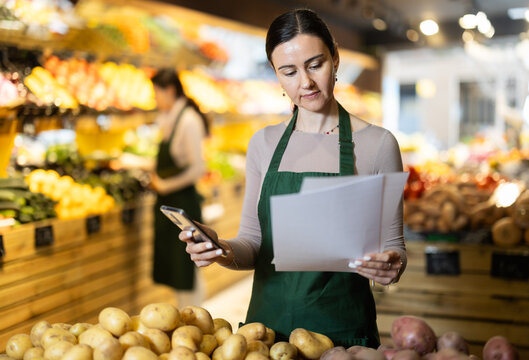 Female owner of vegetable store analyzes documents, reads report. End of current quarter, finalization of sales results