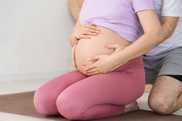 Sporty pregnant couple touching belly at gym, closeup