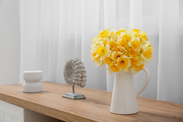 Vase with narcissus flowers and decor on dresser near window in living room, closeup